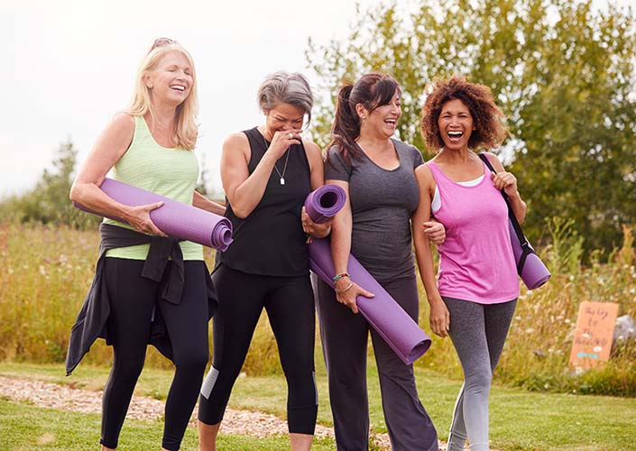 Four midlife women walking together outdoors with yoga mats, smiling and staying active for menopause weight management
