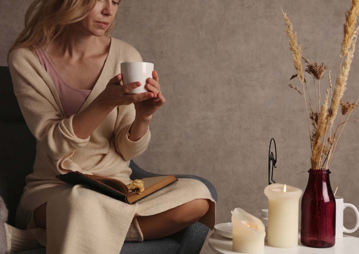 Quiet self-care ritual for women in midlife - holding a warm mug with a book and candle nearby, perimenopause-friendly slow living.